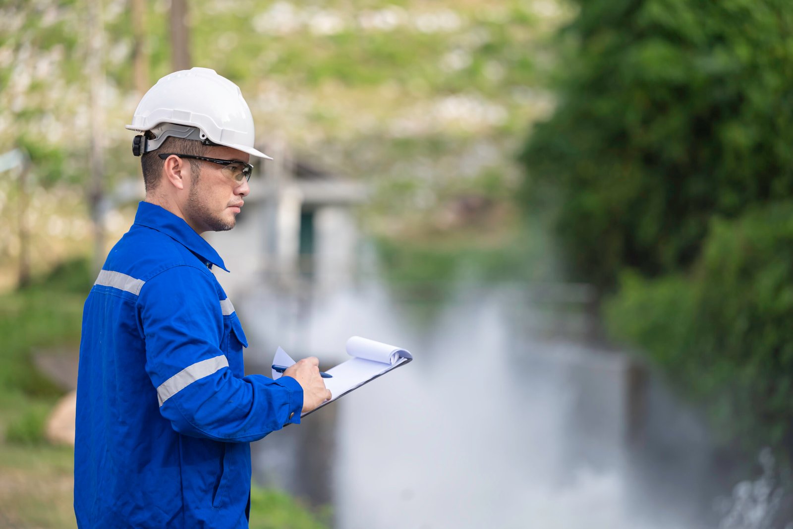 A engineering doing his checking routine. He is wearing hard hat and engineer uniform.Standing by the rail by the dam.Monitor water levels from the heavy rain that has been falling for several days.