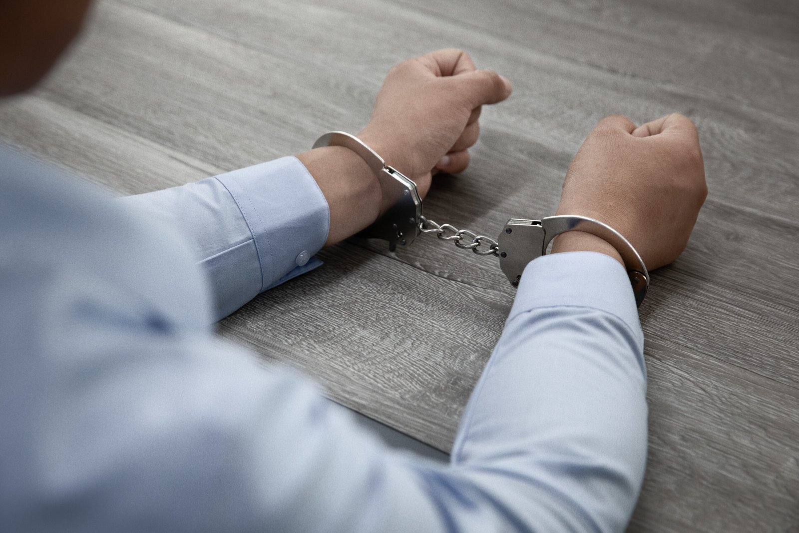 A selective focus shot of male hands in handcuffs on a wooden table