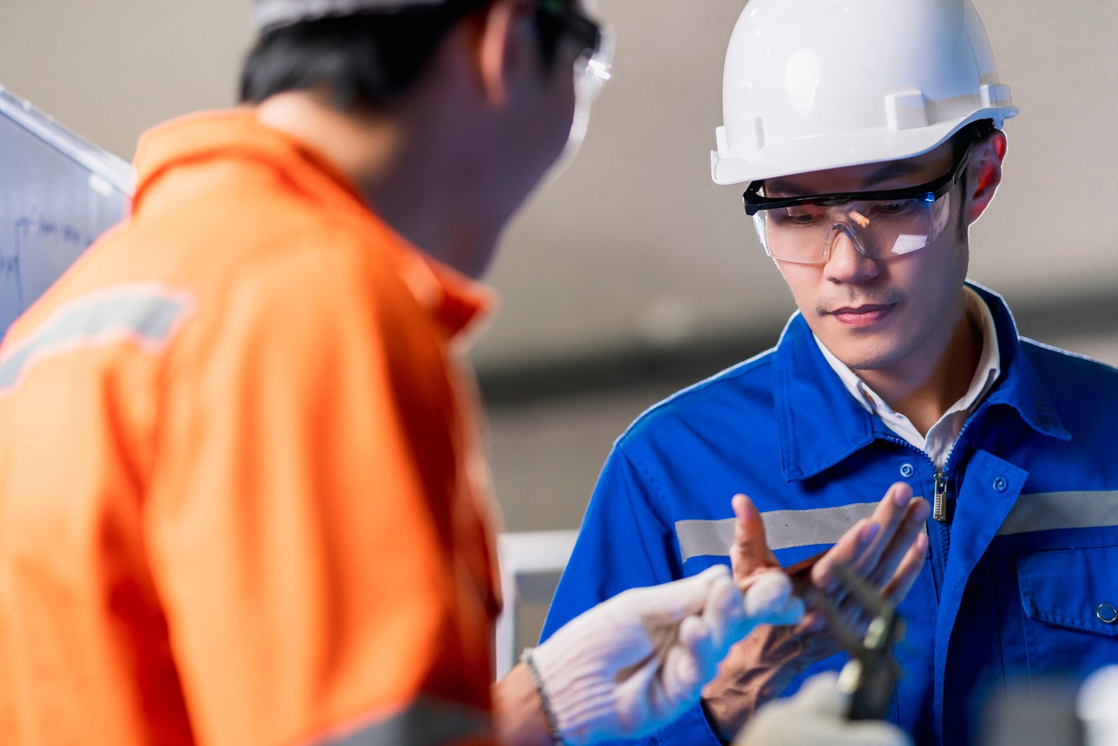 Male Asian engineer professional having a discussion standing by the machine in the factory ,two asian coworker brainstorm explaining and solves the process curcuit mother board of the machine