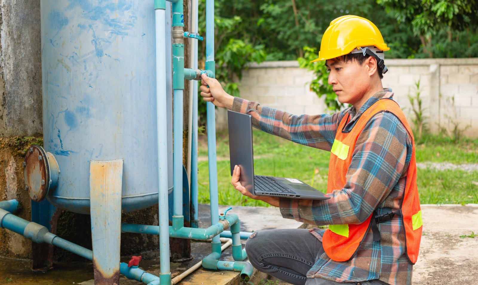 Engineer working in drinking water factory using a laptop computer to check water management system and boiler water pipe outside the factory