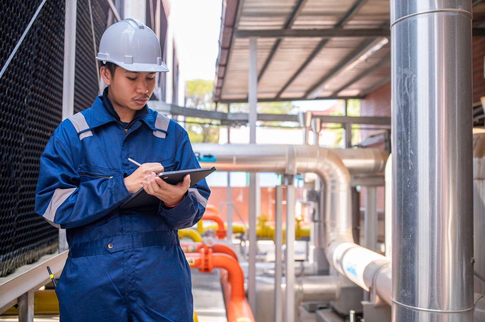 Young engineer working at large factory,Technician in protective uniform and with hardhat  checking temperature in pipes