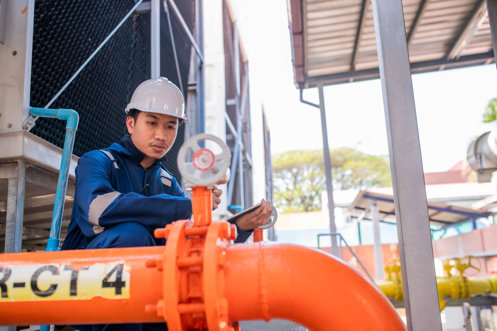 Young engineer working at large factory,Technician in protective uniform and with hardhat  checking temperature in pipes